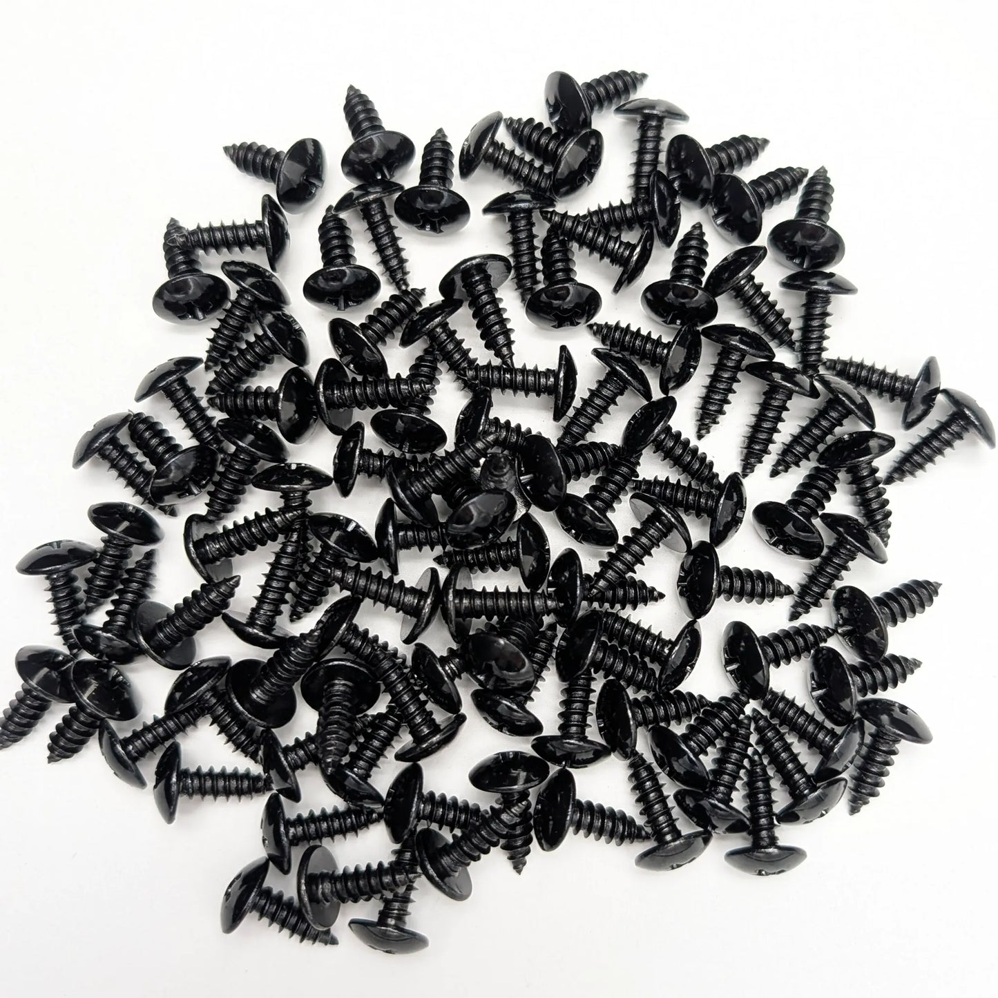 A pile of 100 5/8" black stainless steel truss-head screws, scattered on a white background.