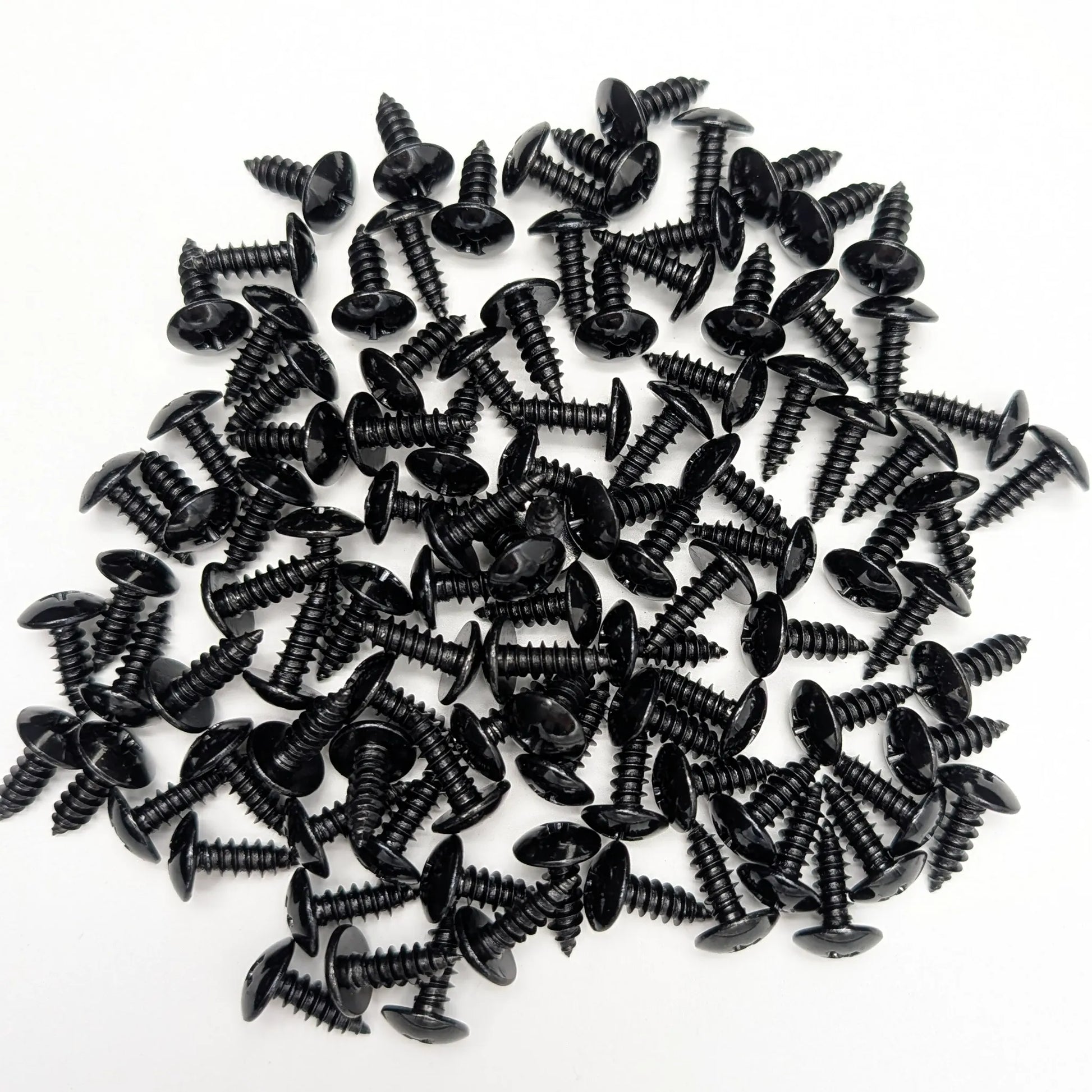 A pile of 100 5/8" black stainless steel truss-head screws, scattered on a white background.