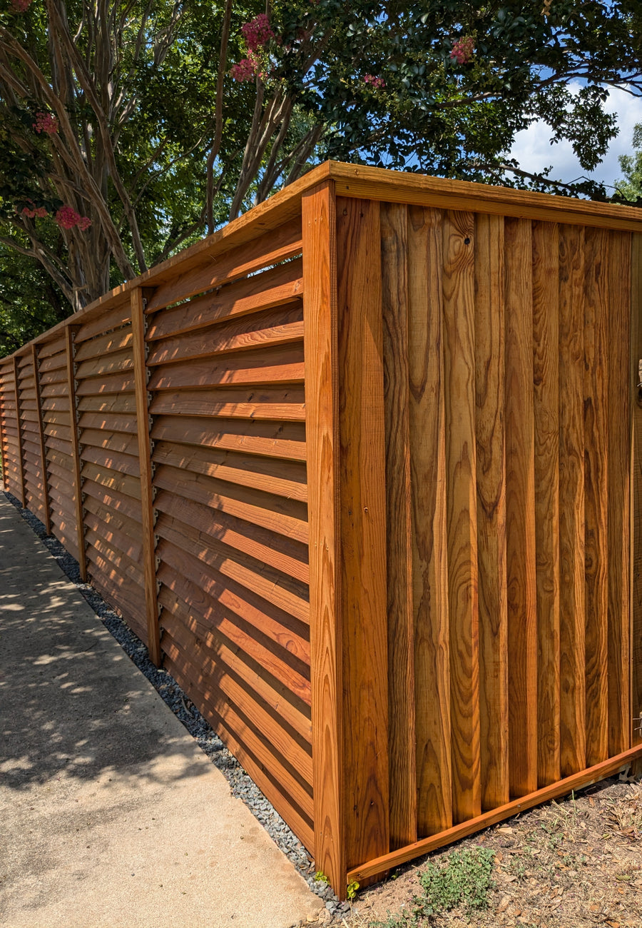 Vertical louvered wood fence installation providing privacy while maintaining airflow in a backyard.